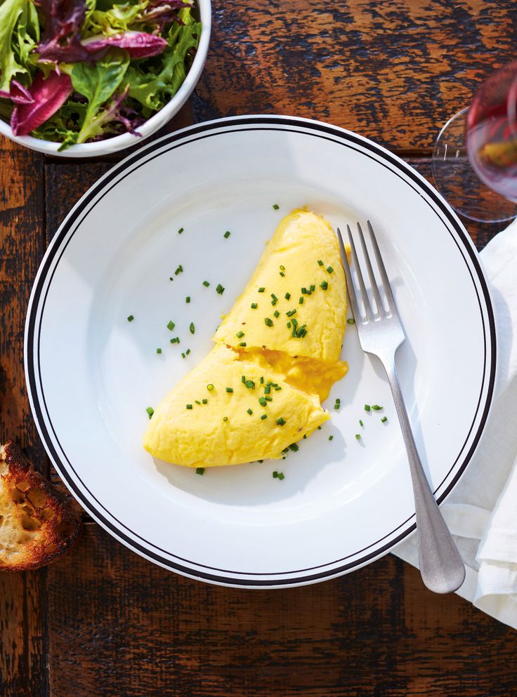 an omelet on a white plate next to a bowl of salad and a glass of wine