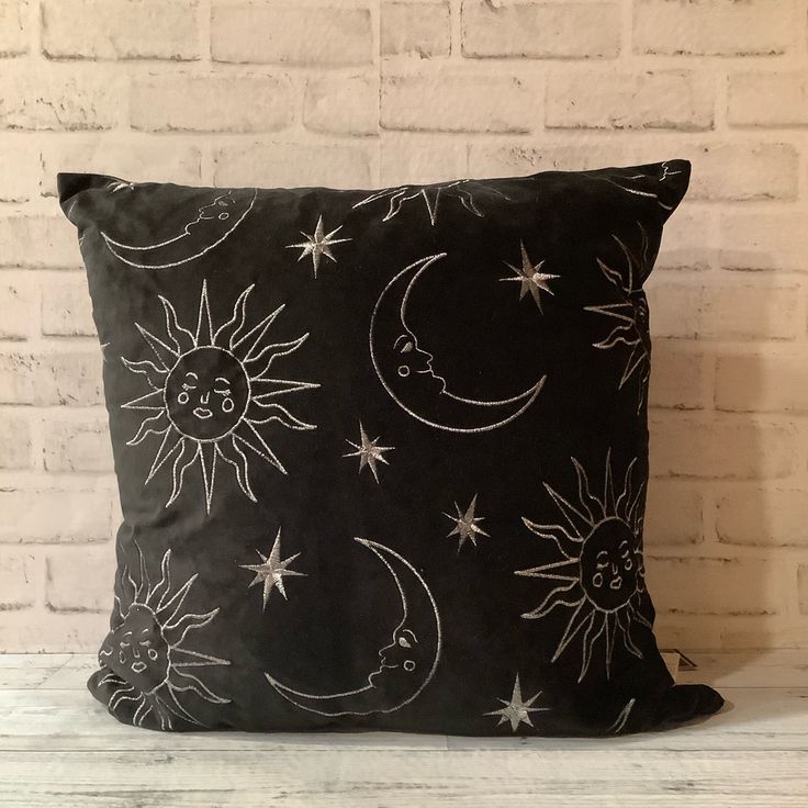 a black pillow with white stars and the moon on it, against a brick wall