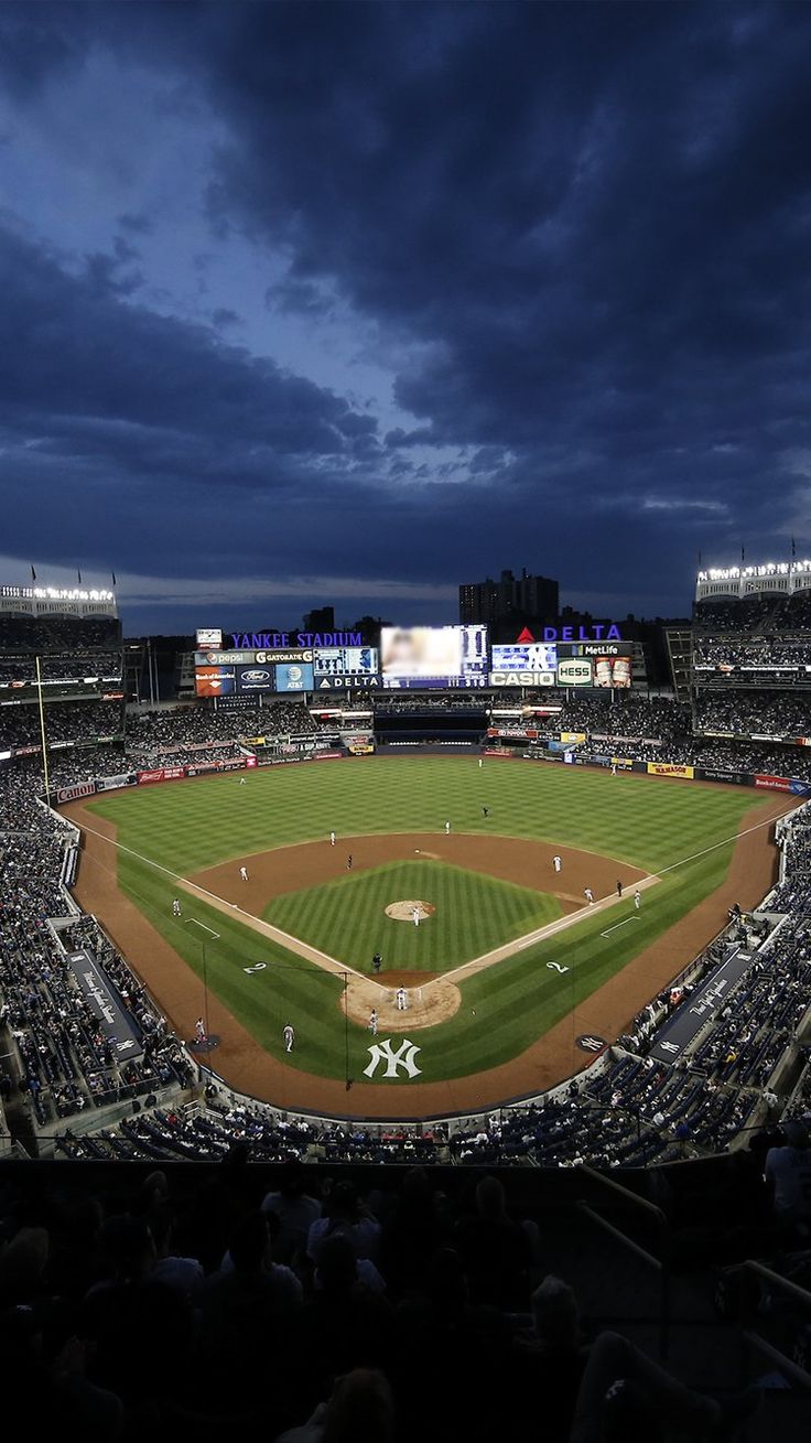 a baseball stadium filled with lots of people on top of a lush green field at night