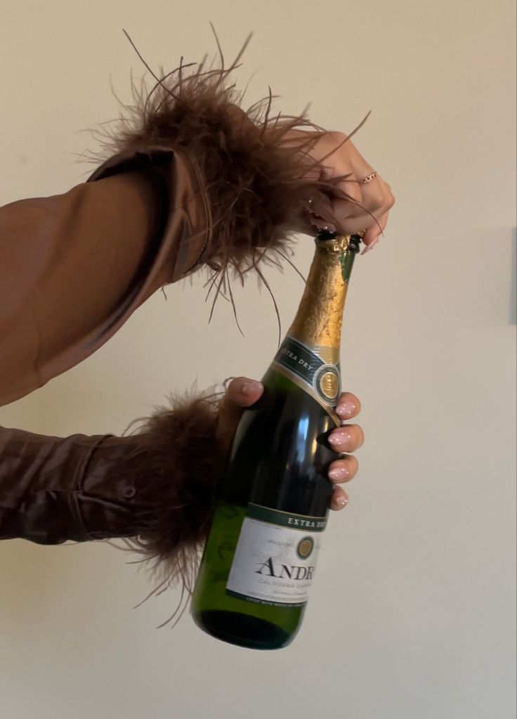 a person holding a bottle of wine in their hand and wearing a furry brown coat