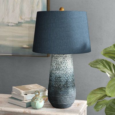 a blue lamp sitting on top of a wooden table next to a plant and books