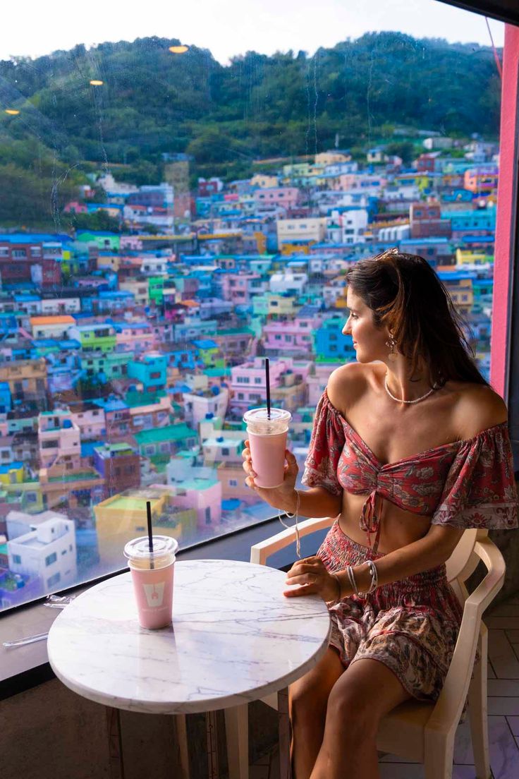 a woman sitting at a table with a drink in her hand looking out the window