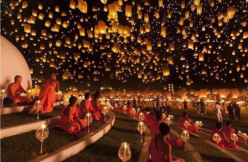 many people are sitting on the ground with lanterns in the sky