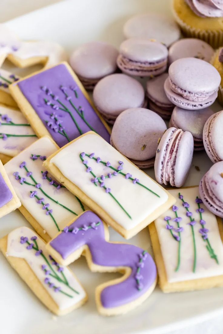 decorated cookies and cupcakes on a white tray with purple frosted icing