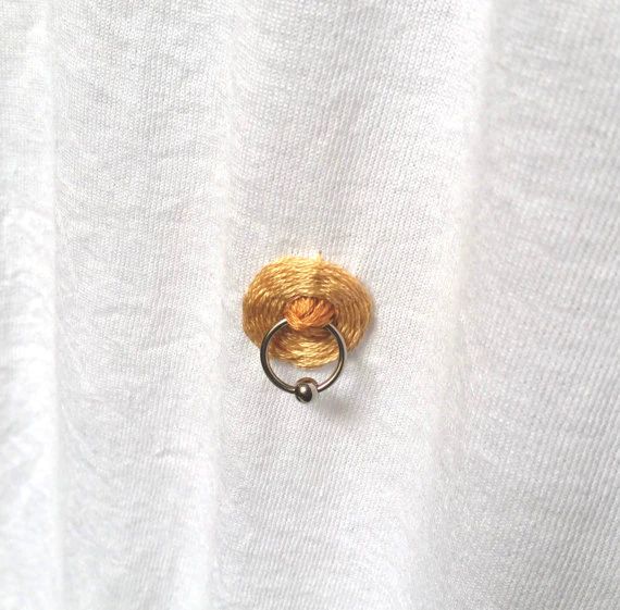 a white shirt with a gold ring on it's left side and an orange object in the middle