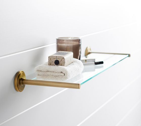 a glass shelf with towels and candles on it next to a wall mounted toilet paper dispenser