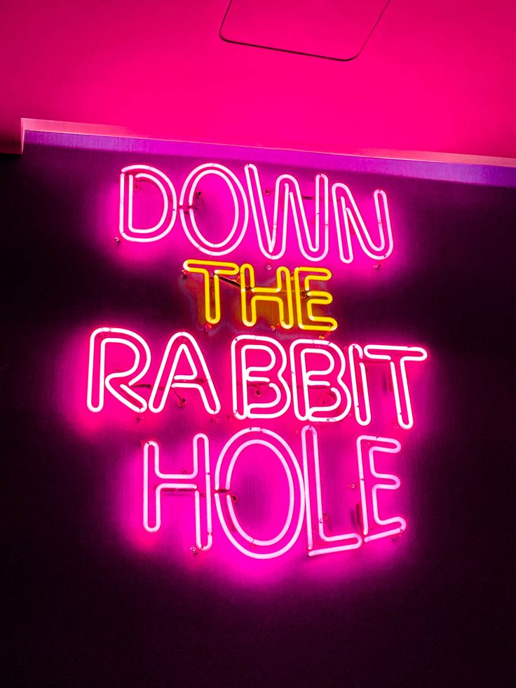 a neon sign with the words down the rabbit hole on it's back wall