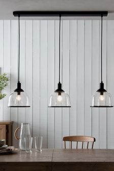 three glass pendant lights hanging over a wooden table