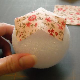 someone is holding a piece of fabric on top of a white ball with red flowers