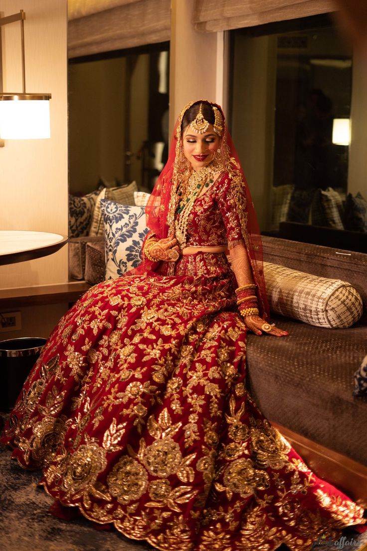 a woman sitting on top of a couch in a red and gold wedding dress,