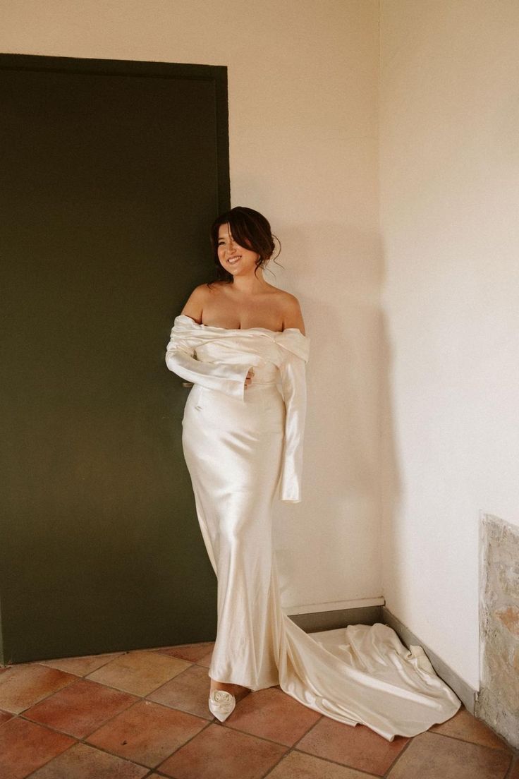 a woman in a white dress leaning against a wall