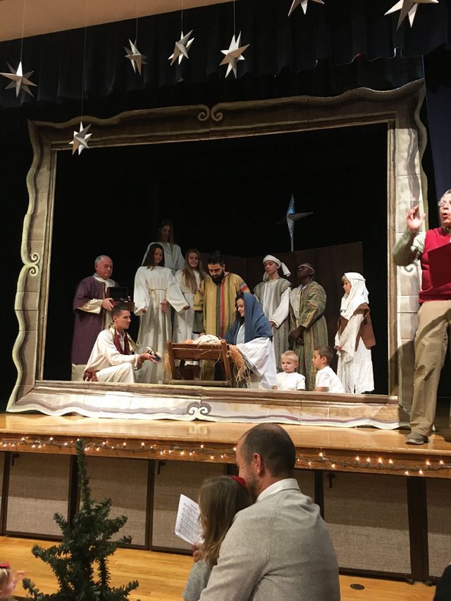 a group of people standing on top of a stage next to a baby jesus in a crib