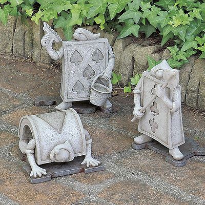 three little statues sitting on top of a stone floor next to green plants and shrubbery