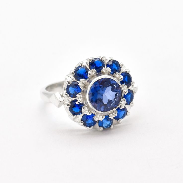 Sapphire Flower Ring set with Created Sapphire in a diamond cut & stunning blue color, at sizes 7mm and 3mm (2 Cts combined). Solid 925 Sterling Silver ☞ made to last. Click here for ☞ Flower CollectionDetails:• Created Sapphire in a stunning blue color• Sapphire Center Stone: 7mm, 1 Ct, diamond cut• Small Sapphires: 3mm each, 1 Ct total, diamond cut• Dimensions: Band width ≈ 2.3mm, thickness ≈ 1.3mm• Solid 925 Sterling SilverSKU 2243 Blue Gemstone Flower Ring Gift, Gift Blue Gemstone Flower Ring, Classic Flower Gemstone Jewelry, Classic Flower-shaped Gemstone Jewelry, Blue Gemstone Flower Ring, Blue Cluster Ring As A Gift, Blue Cluster Ring For Gift, Classic Round Gemstone Flower Ring, Blue Cluster Ring Gift Round Cut