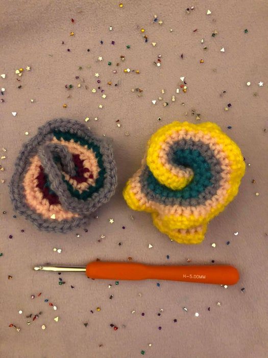 two crocheted objects are next to a knitting needle on a table with confetti sprinkles