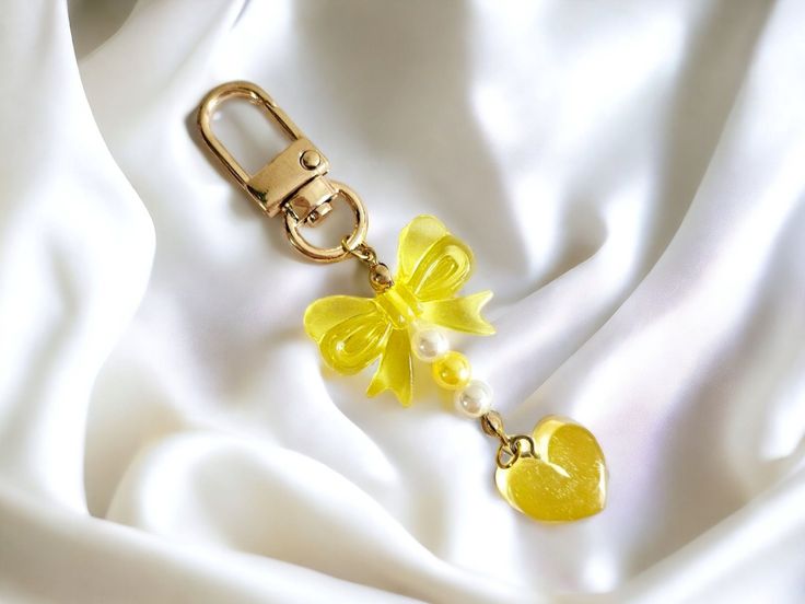 a yellow flower and heart charm on a white satin background with a gold metal keychain