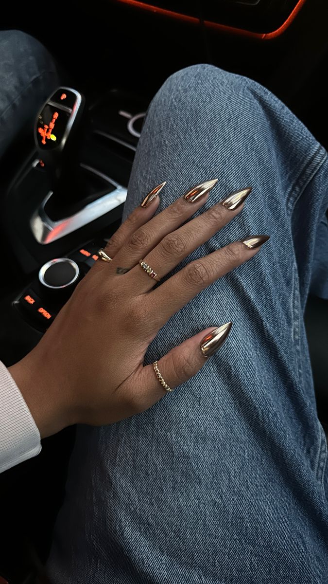 Gold chrome gel-x medium stiletto nails on a black girl’s hand while wearing gold jewelry and rings Nails Dark Skin, Chrome Nail Colors, Black Chrome Nails, Gold Chrome Nails, Bronze Nails, Gold Acrylic Nails, Nails Dark, Chrome Nails Designs, Metallic Nails