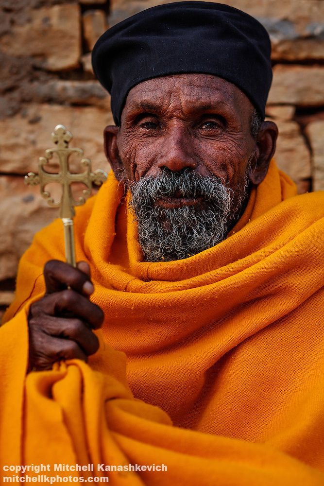 an old man with a cross in his hand and wearing a yellow scarf around his neck