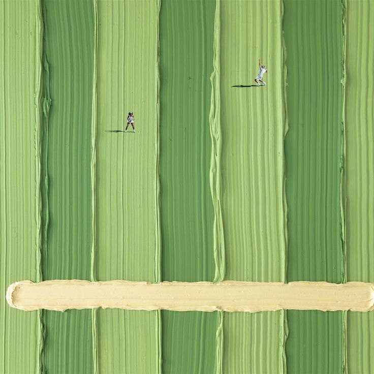 two people are walking on the grass in front of a green wall with vertical lines