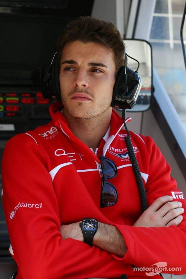 a man in a red jacket with headphones on and his arms crossed looking at the camera