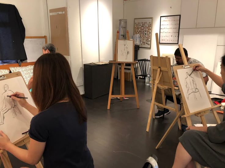 three people sitting in front of easels drawing on paper