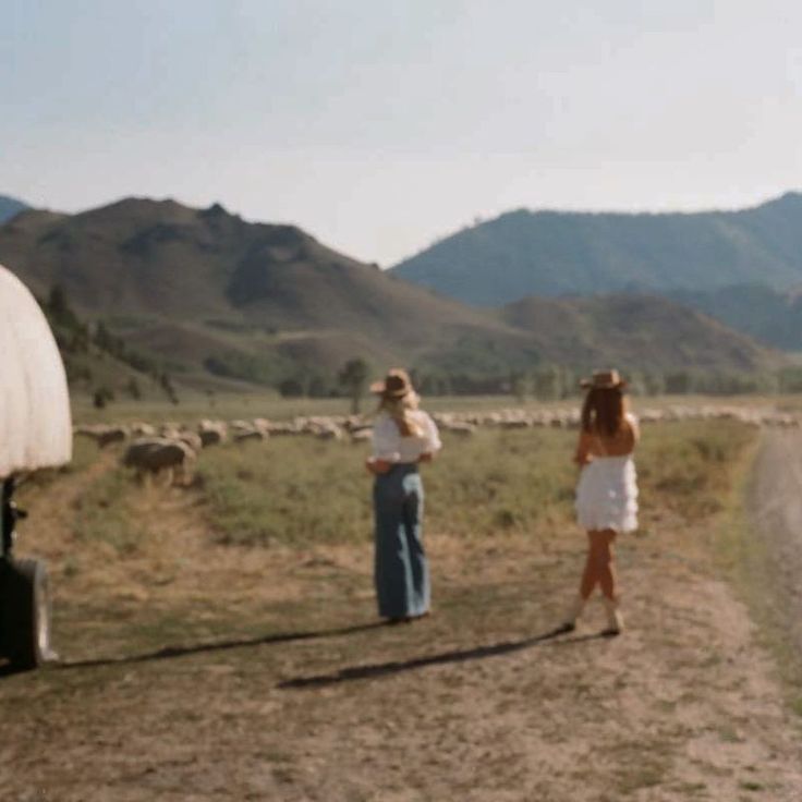 two women standing on the side of a dirt road