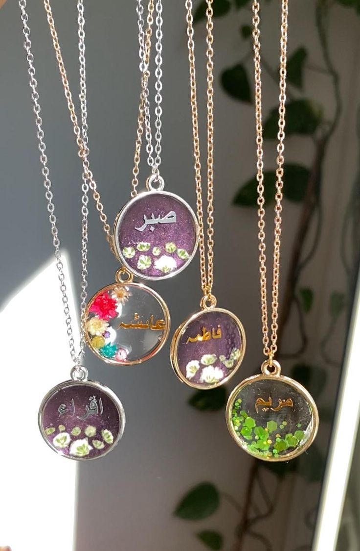 four different necklaces hanging from a chain on a window sill in front of a potted plant