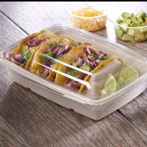 a plastic container filled with tacos and limes on top of a wooden table