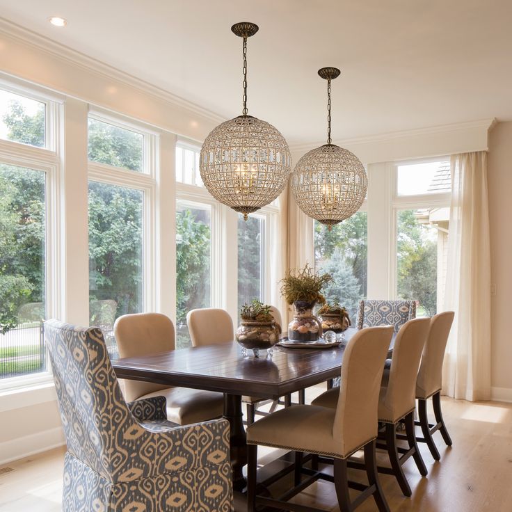 a dinning room table and chairs with chandelier hanging from the ceiling in front of large windows