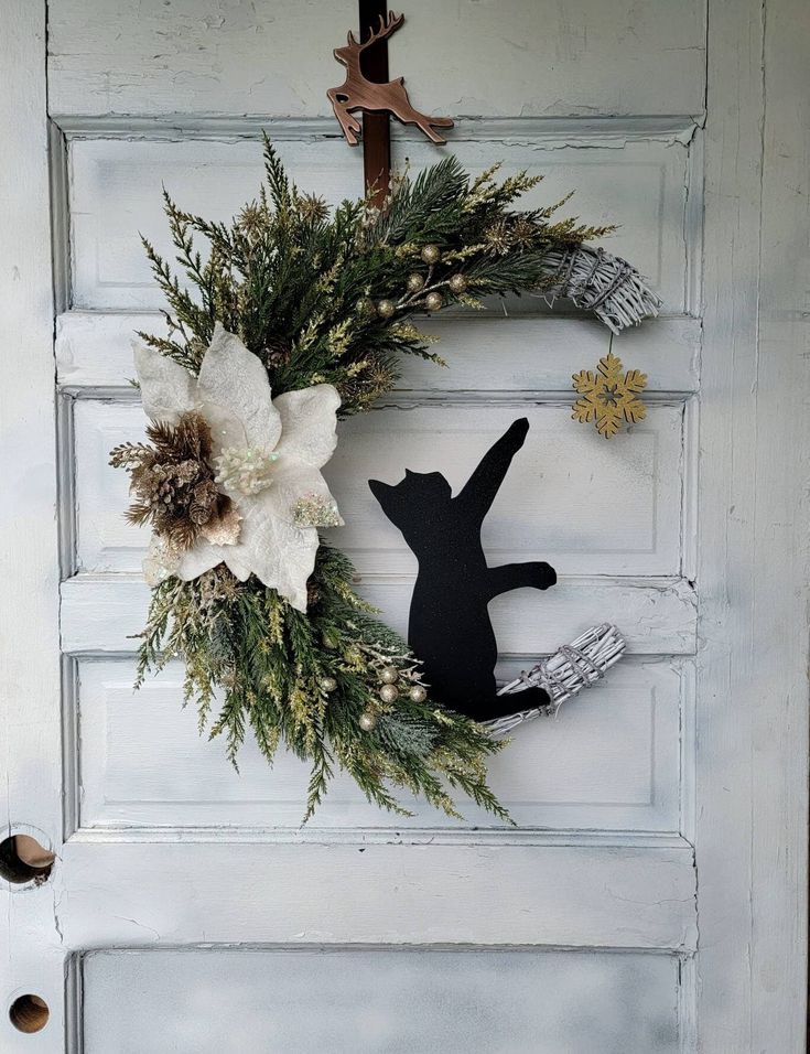 a black cat is hanging on the front door with white flowers and pineconis