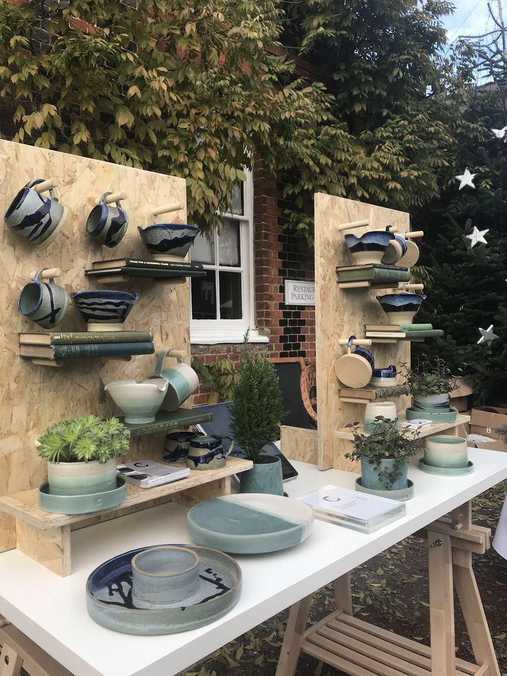 a table with plates and bowls on it in front of a brick building, surrounded by greenery