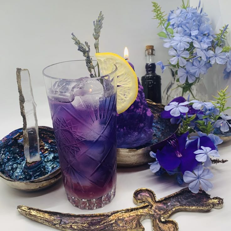 there is a purple drink with lemon and blue flowers on the table next to it