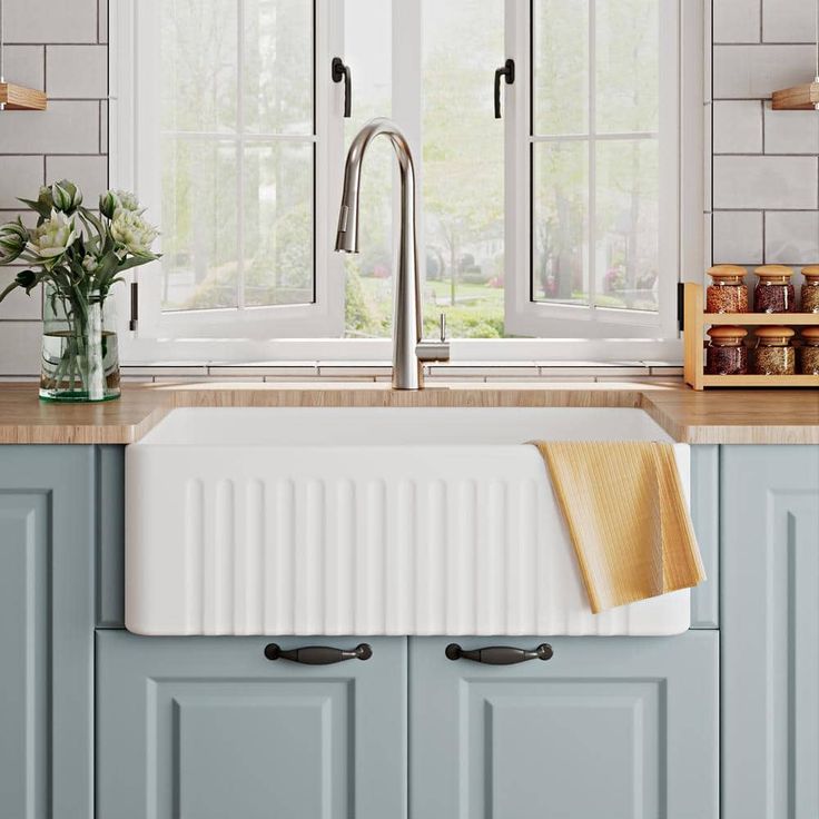 a kitchen sink sitting under a window next to a counter top with flowers on it