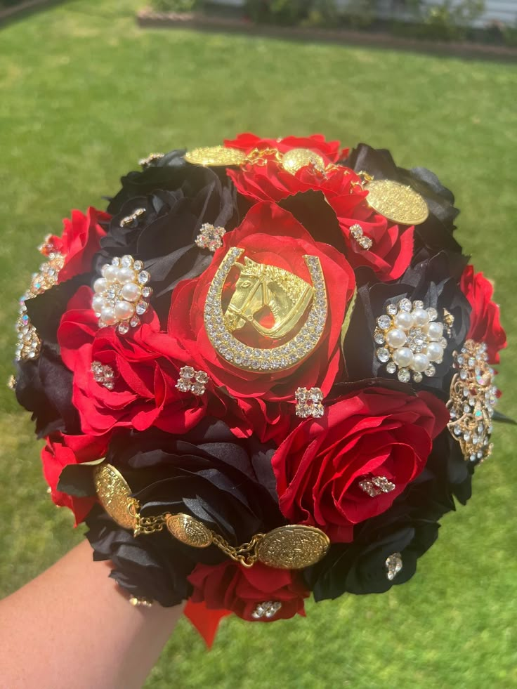 a bridal bouquet made with red and black flowers in the middle of someone's hand