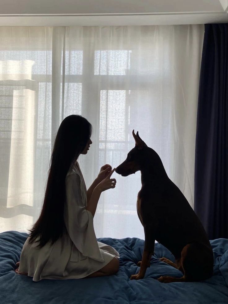 a woman sitting on a bed petting a dog's nose with her hand