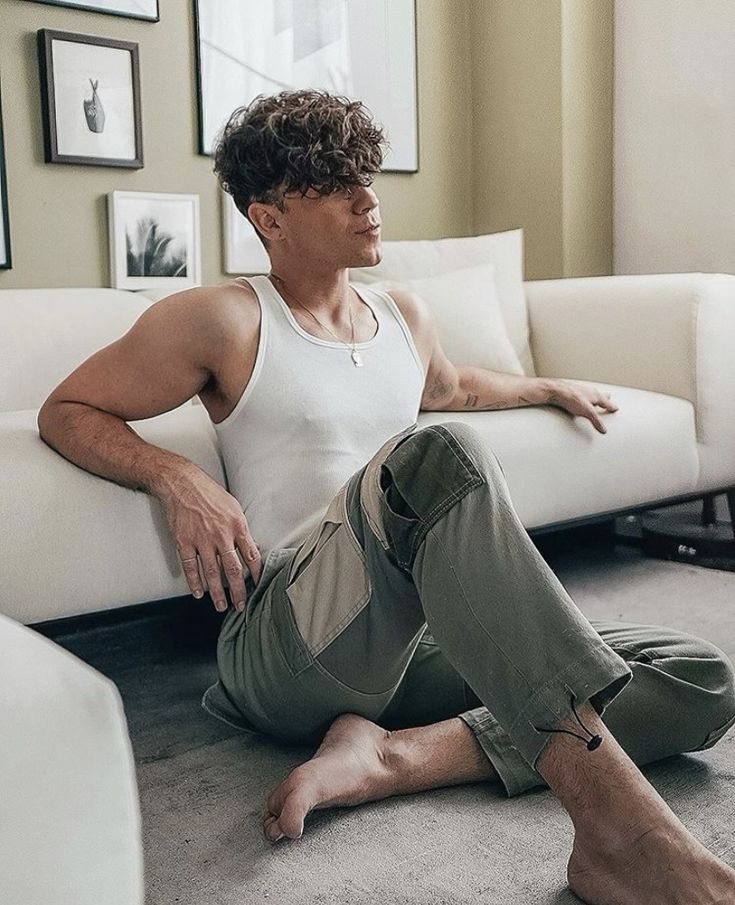 a man sitting on the floor in front of a white couch with his legs crossed