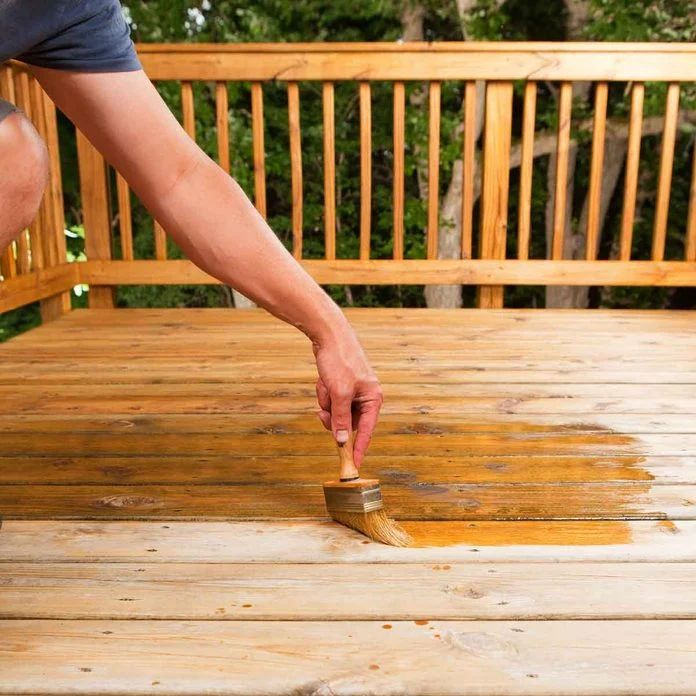 a person is painting a wooden deck with a paintbrush and some brown stain on it