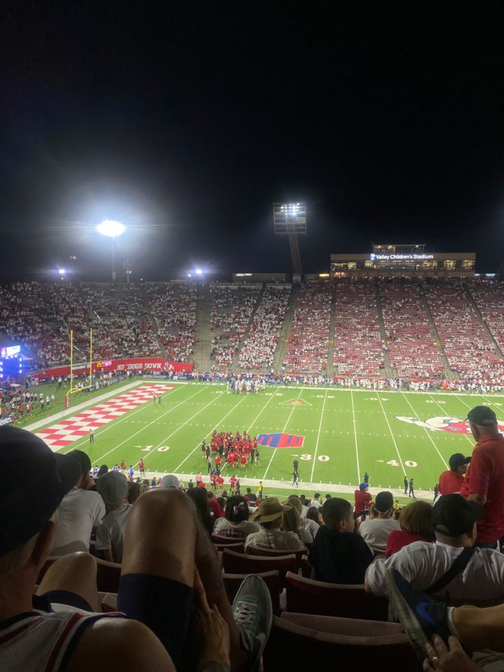 a football stadium filled with lots of people sitting on the bleachers at night