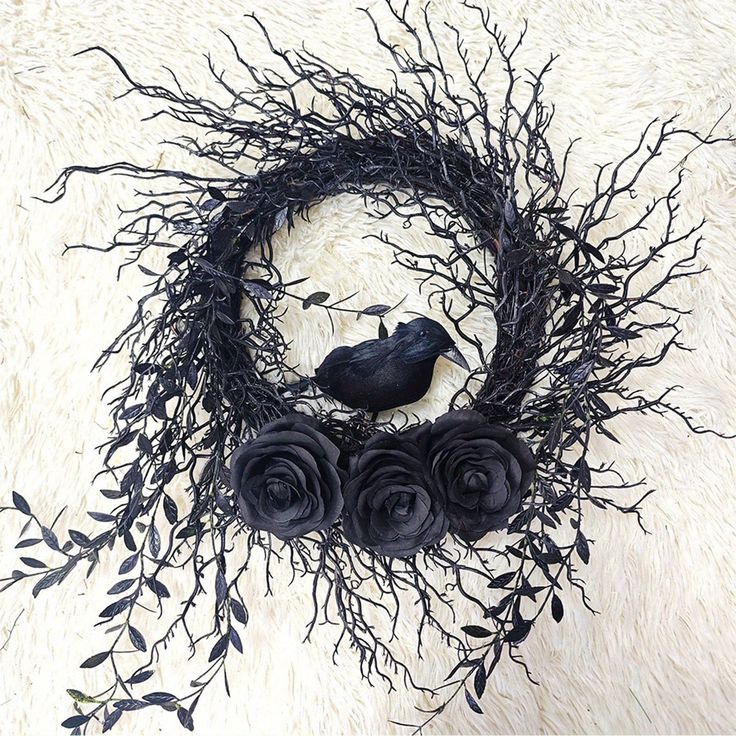 a black bird sitting on top of a tree branch wreath with roses and twigs around it