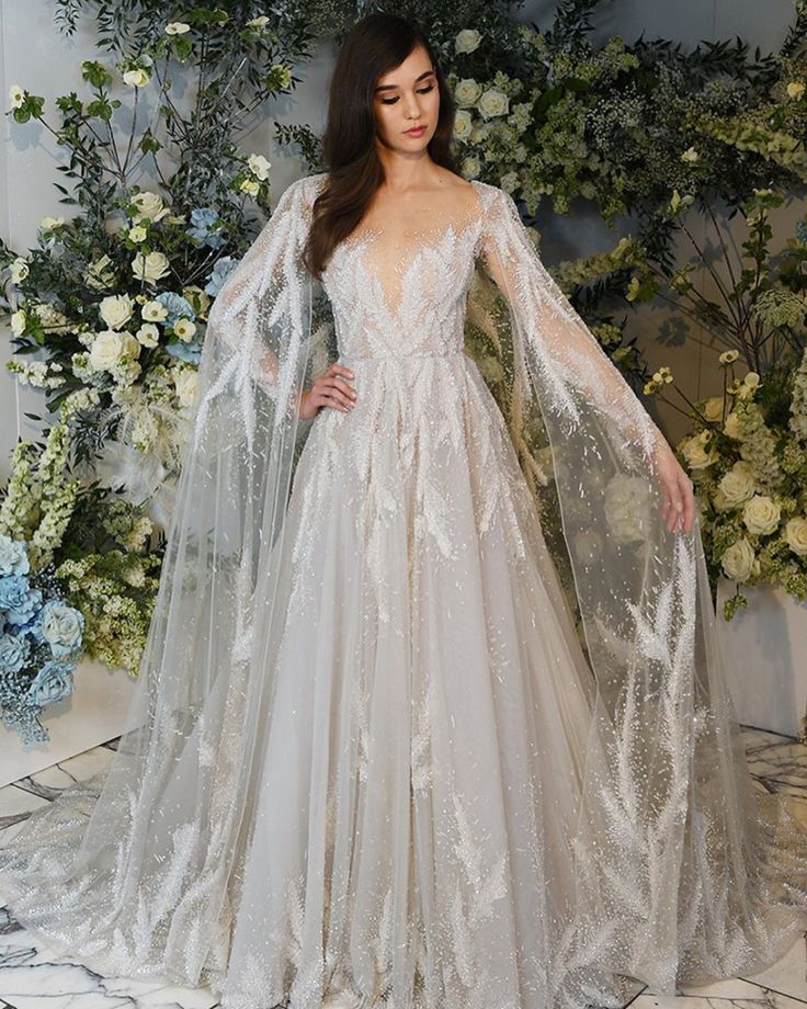 a woman in a wedding dress standing next to a flower wall with flowers on it