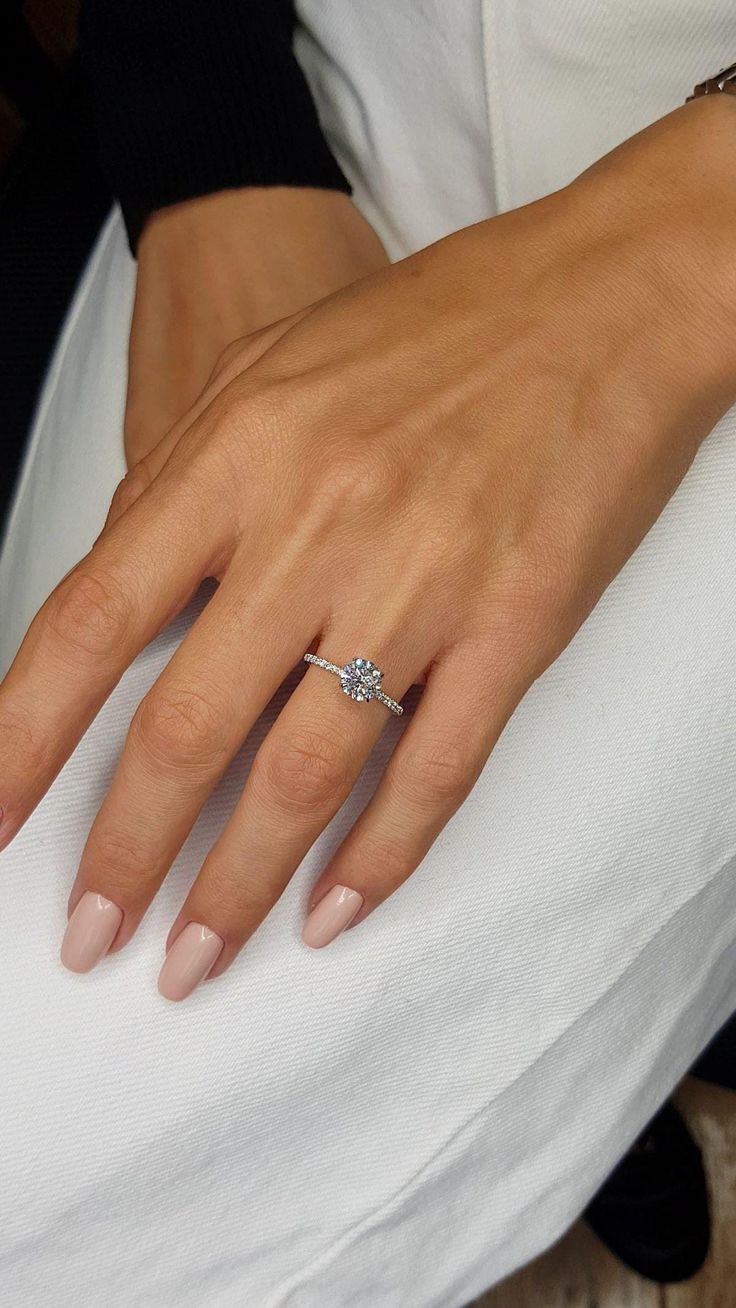 a woman's hand with a diamond ring on her left hand, sitting on a white pillow