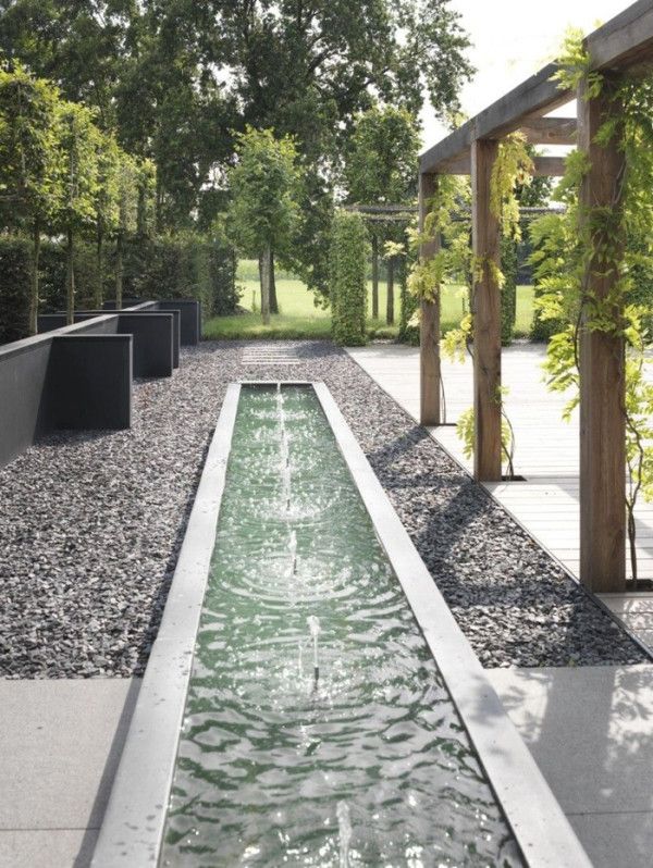 an outdoor water feature in the middle of a walkway with trees and bushes around it