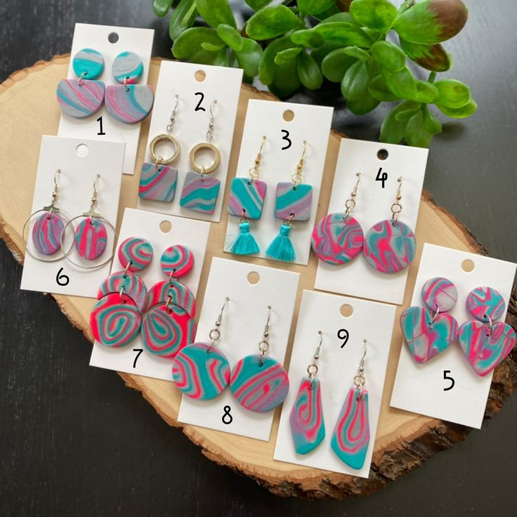 several pairs of earrings on display in front of a wooden slice with price tags for each pair