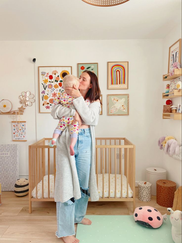 a woman holding a baby in her arms while standing in front of a crib