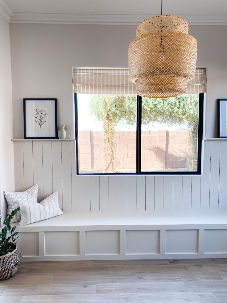 a room with white walls and wood paneling on the wall, a bench in front of a large window