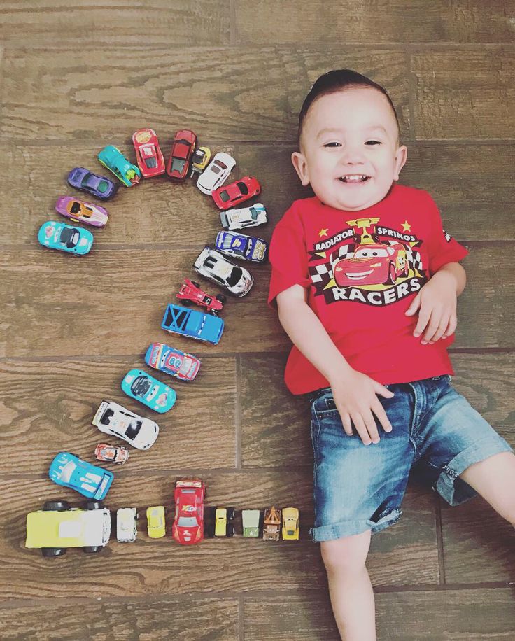 a young boy laying on the floor with toy cars in front of him and smiling at the camera