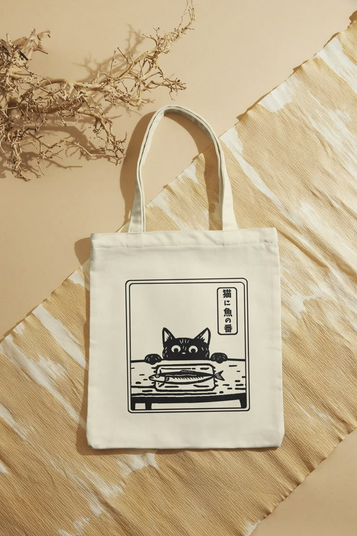 Our cute cat and fish design tote bags are made from cotton canvas material. This environment friendly tote bag is perfect for your daily use to carry essentials, groceries, or books. The cute Japanese style design brings a touch of cultural charm to your outings! The writing is a Japanese proverb and it translates "Trusting the cat to watch over the fish." which means it is obvious that the situation is dangerous.    - It is 100% cotton  - Environment friendly - Machine wash cold and inside out Cool Tote Bag Design, Cute Tote Bag Design, Tote Bag Design Ideas, Bag Design Ideas, Japanese Tote Bag, Cat And Fish, Tote Bag Art, Cat Tote Bag, Best Tote Bags