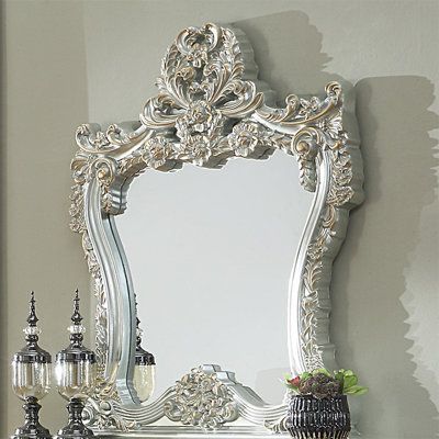 an ornate silver mirror sitting on top of a white dresser next to a vase with flowers