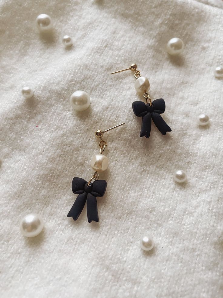 two pairs of earrings with black bows and pearls on white fabric background, closeup