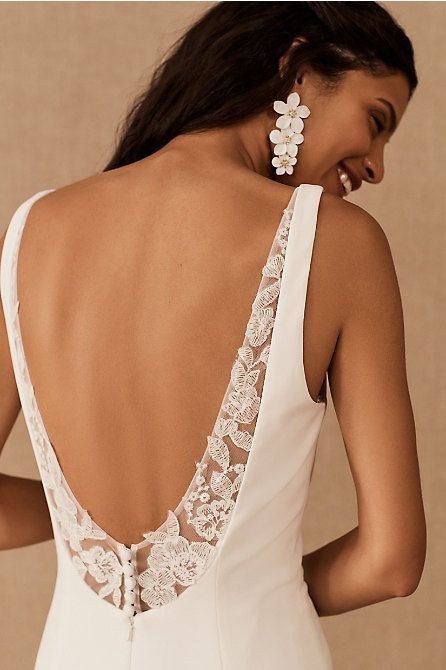 the back of a woman wearing a white wedding dress with lace detailing and flower clip earrings